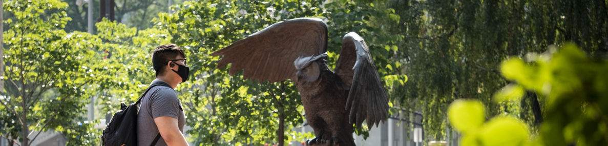 Student wearing a mask walking by Owl statue.